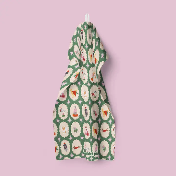 Green Christmas tea towel featuring a repeating pattern of dogs in festive attire within cream oval frames on a green