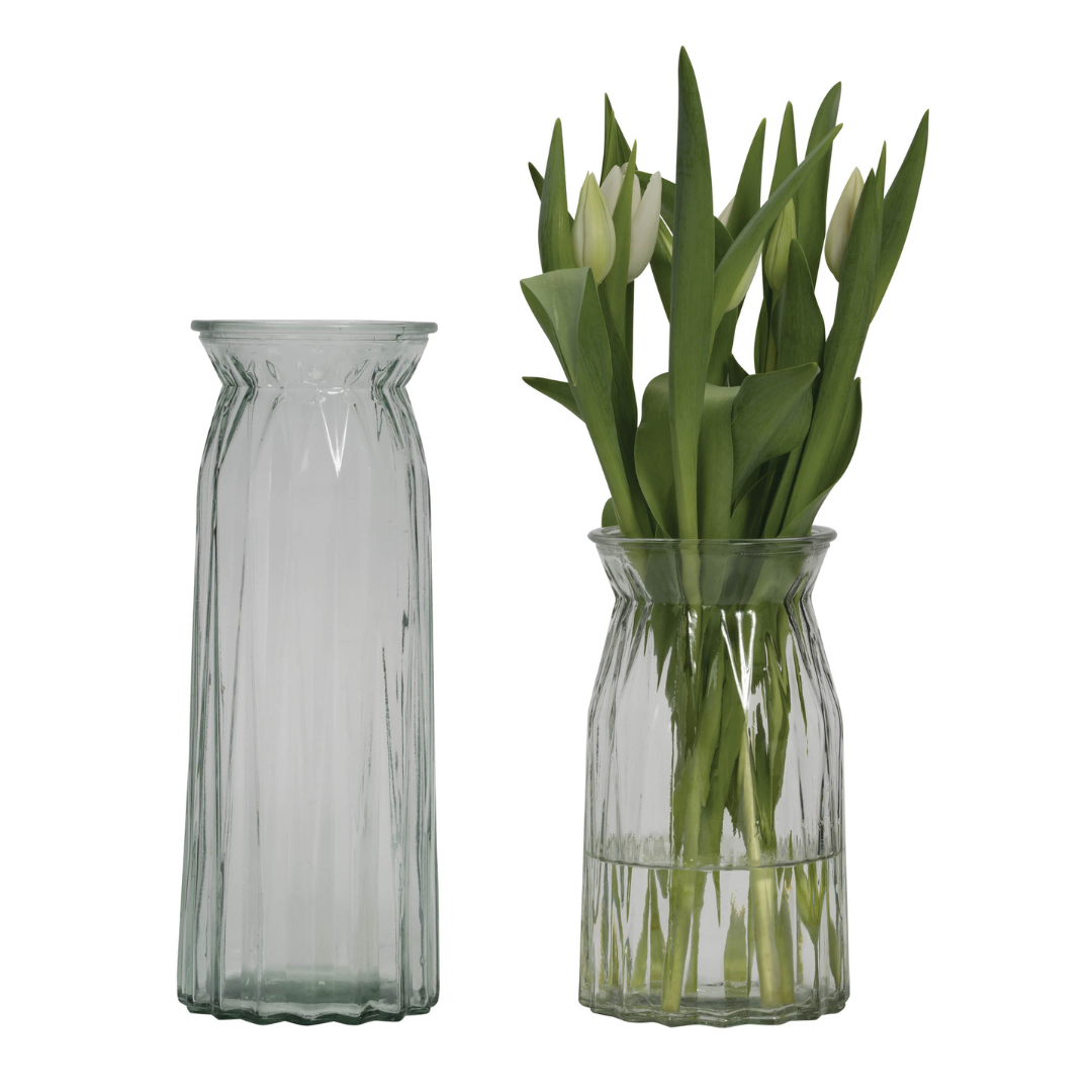 Two clear glass vases with vertical ribbed texture; one vase holds a bouquet of white tulips.