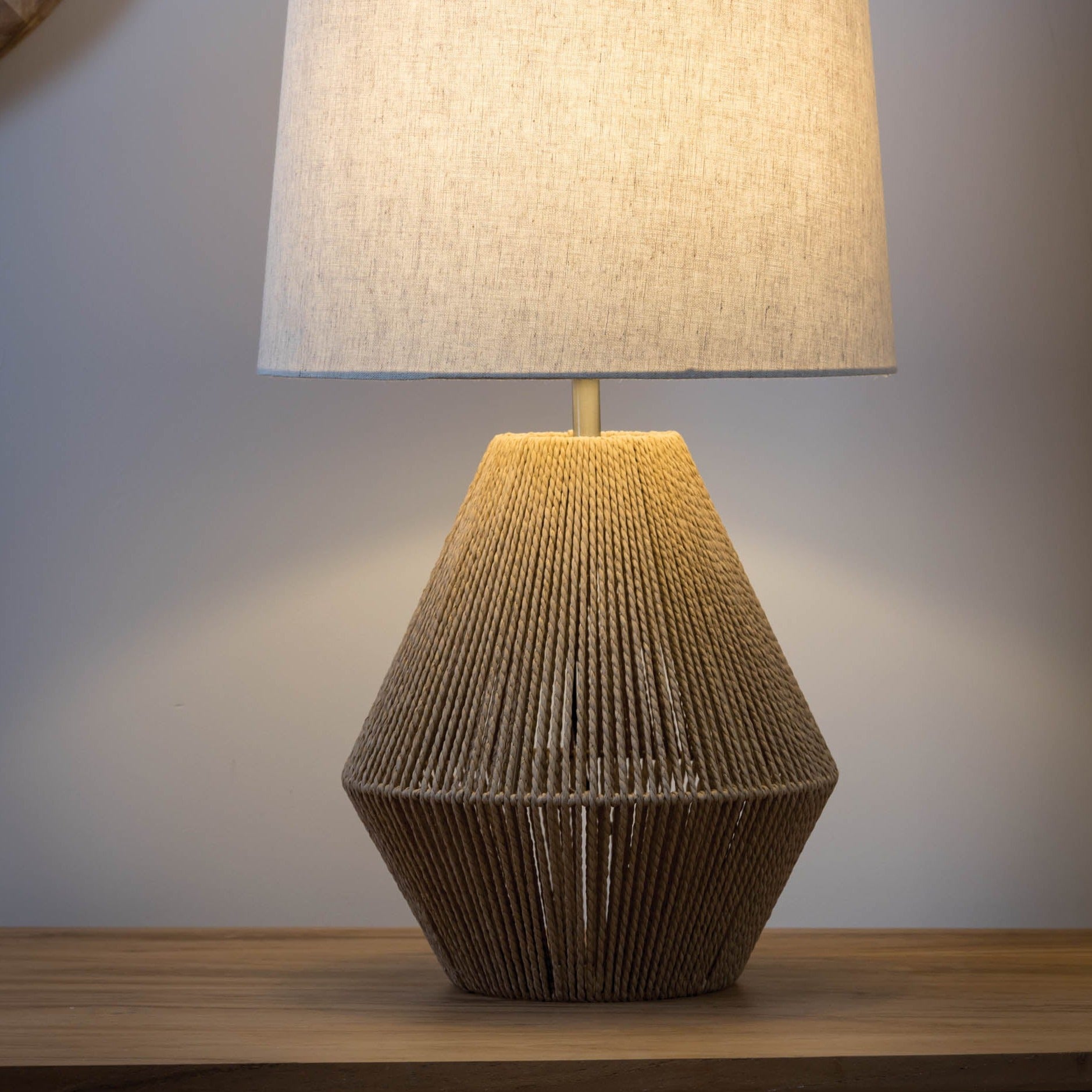 Table lamp with a beige linen shade and a geometric base crafted from light brown rope.