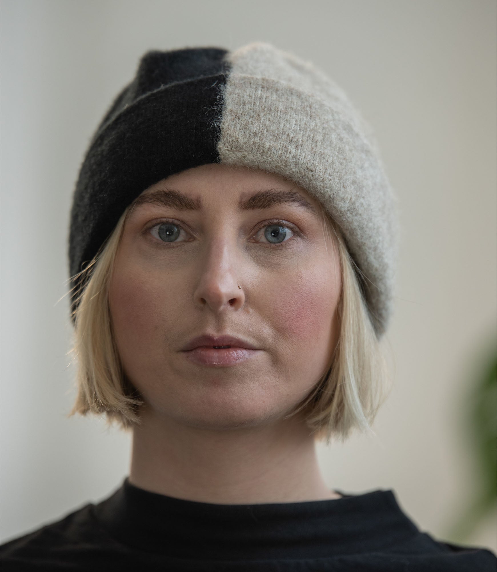 Close-up of a person wearing a half-black, half-beige knit beanie.  The hat is soft and textured.