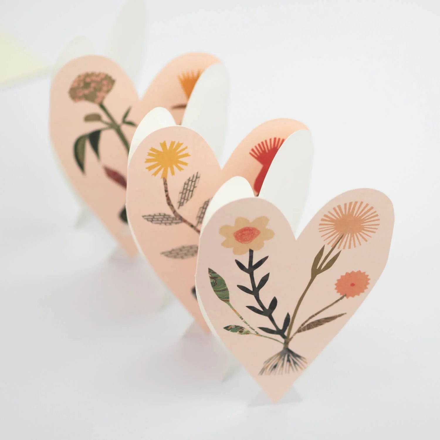 Three interconnected peach-colored paper hearts, each adorned with a unique floral illustration in muted tones.