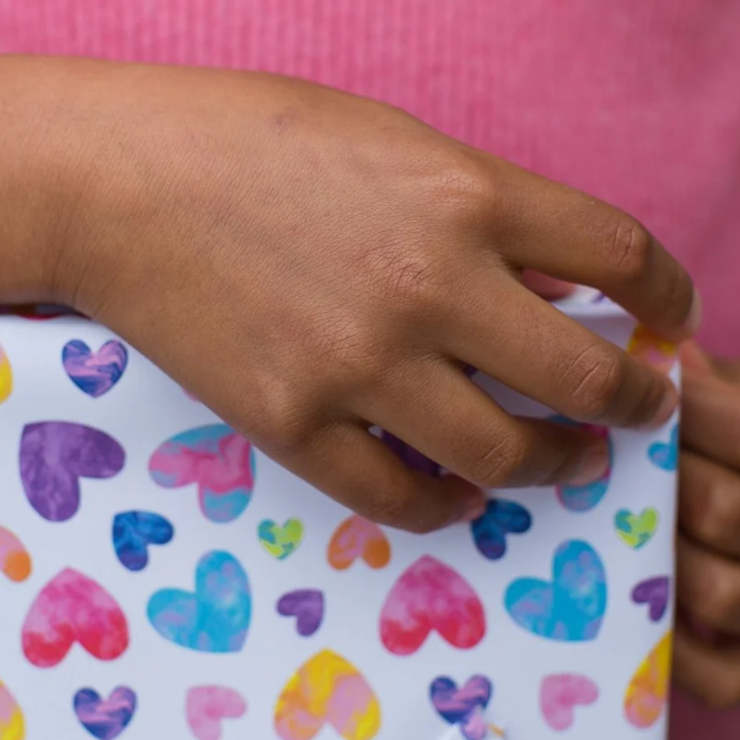 Hand holding a gift bag with a colorful heart pattern.