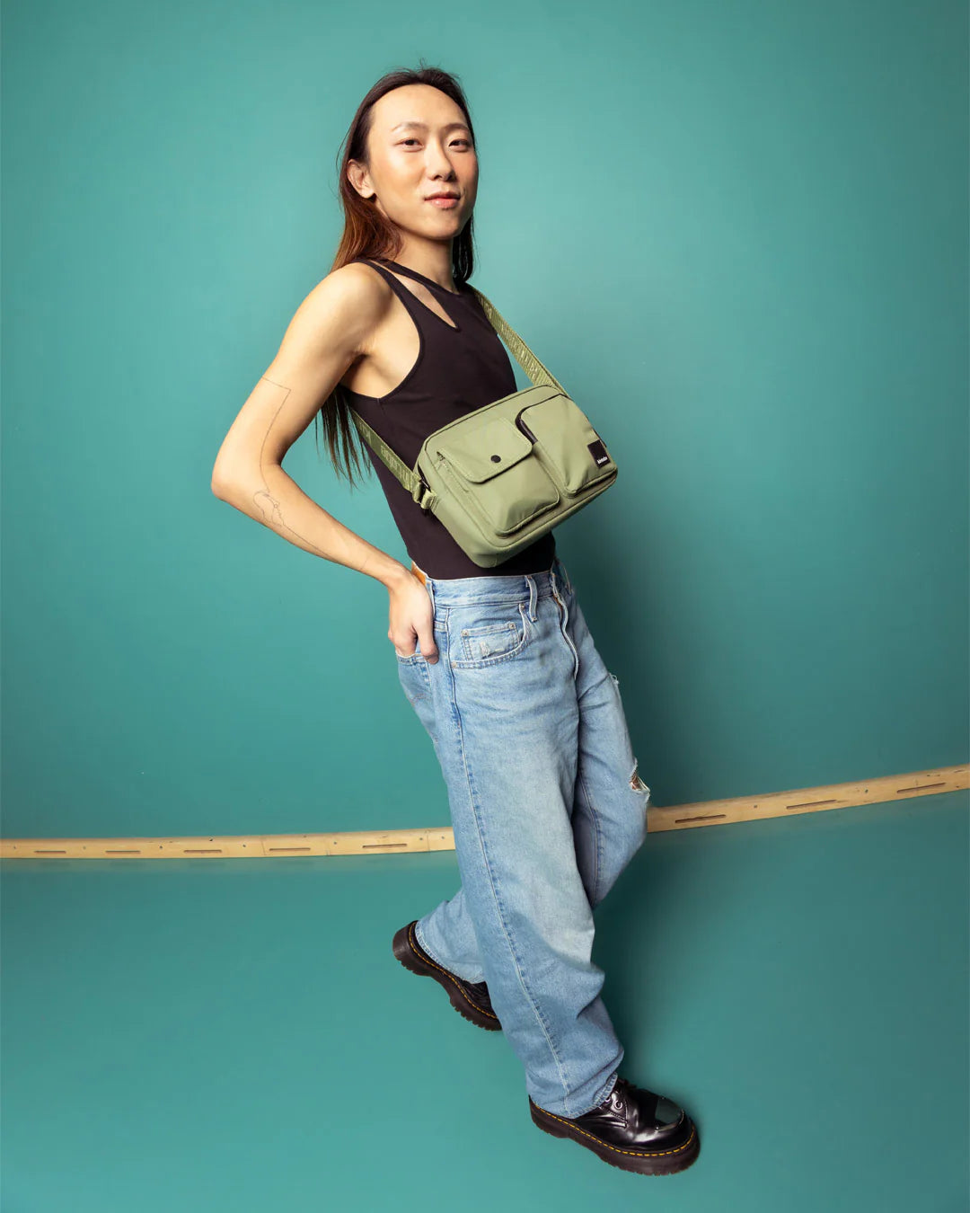 Sage green crossbody bag with multiple compartments, worn by a person in jeans.