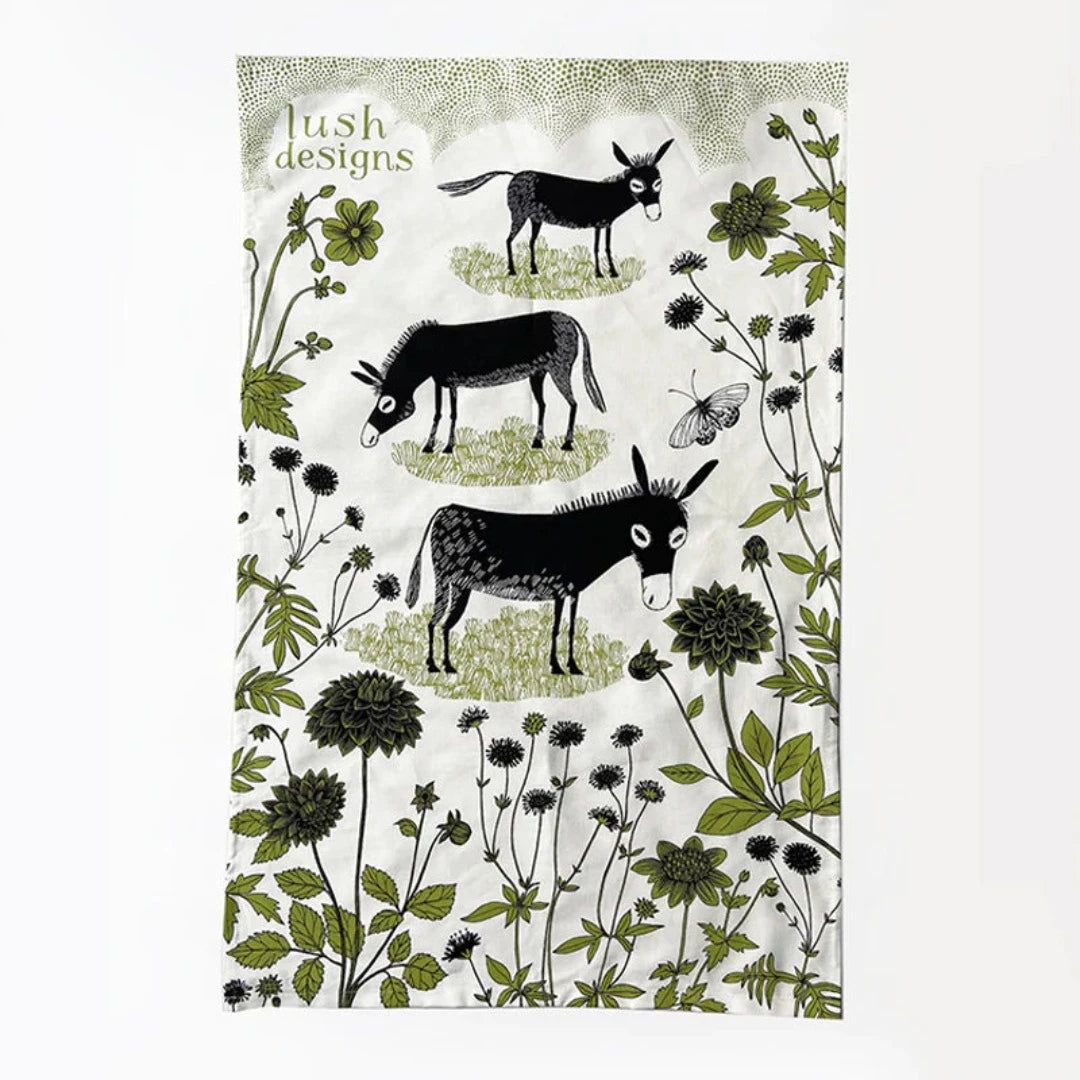 Lush Designs tea towel featuring three black donkeys and green floral illustration on a cream background.