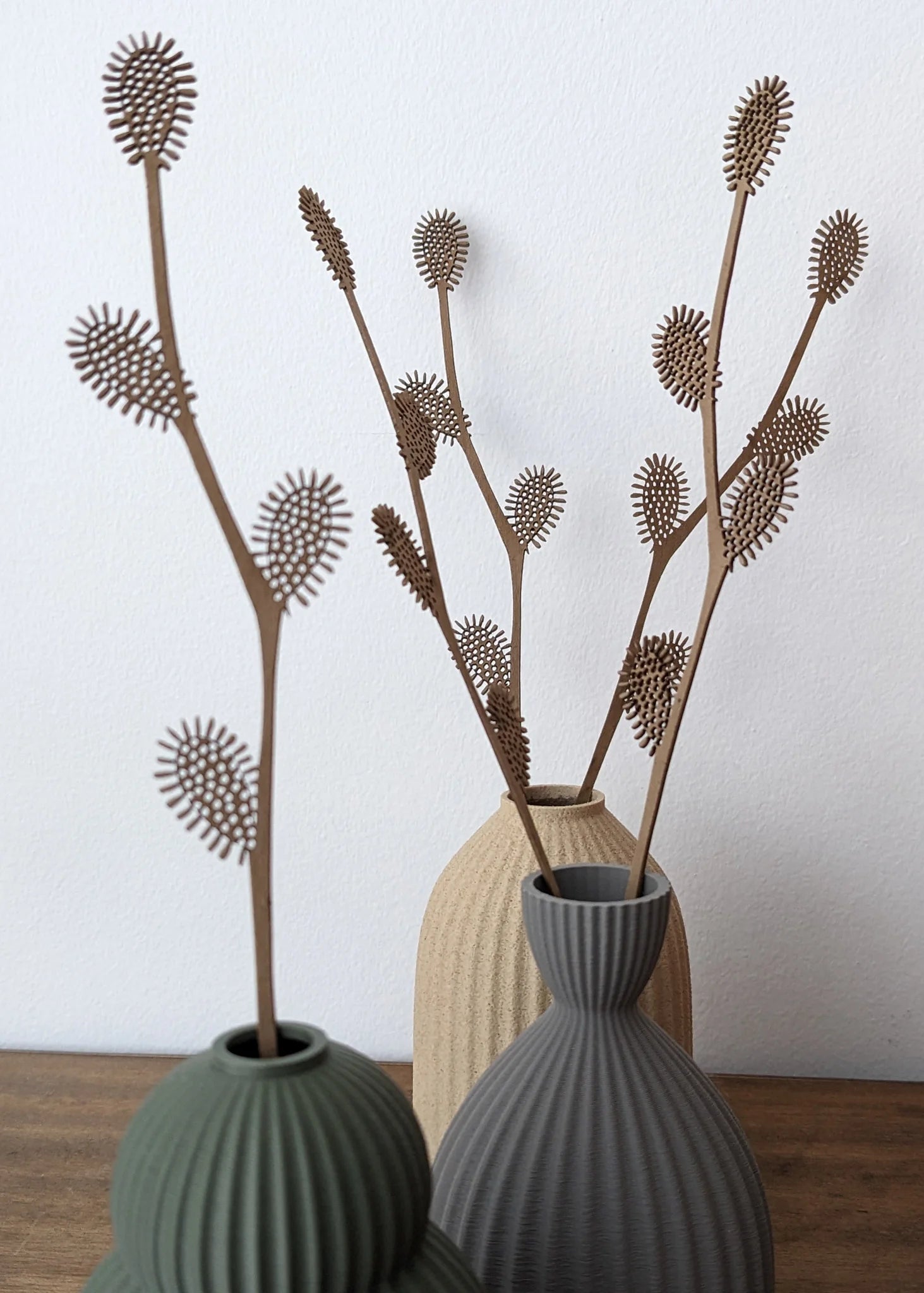 Three textured vases hold decorative brown laser-cut branches with detailed, spiky leaf clusters.