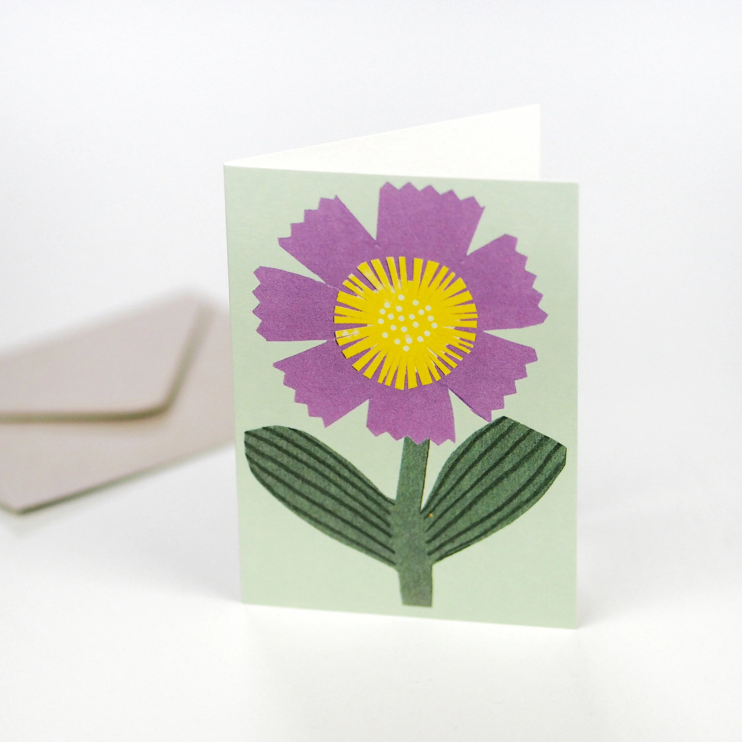 A light green greeting card features a stylized purple flower with a yellow center.