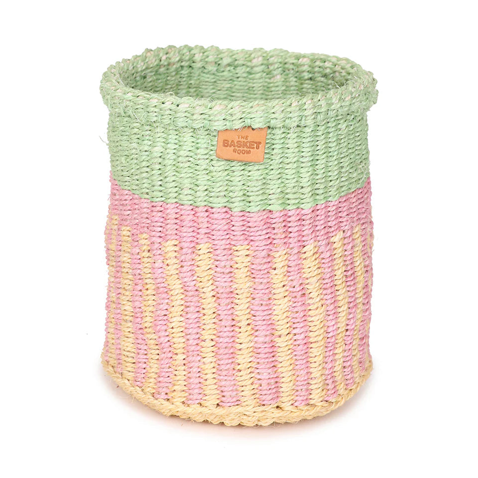 Cylindrical woven basket with a light green top and a pink and pale yellow striped bottom.  Small leather label visible.