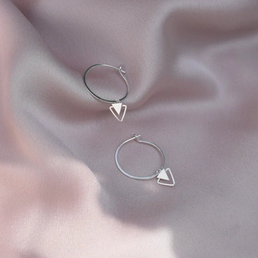 Silver hoop earrings with small, dangling triangle charms.