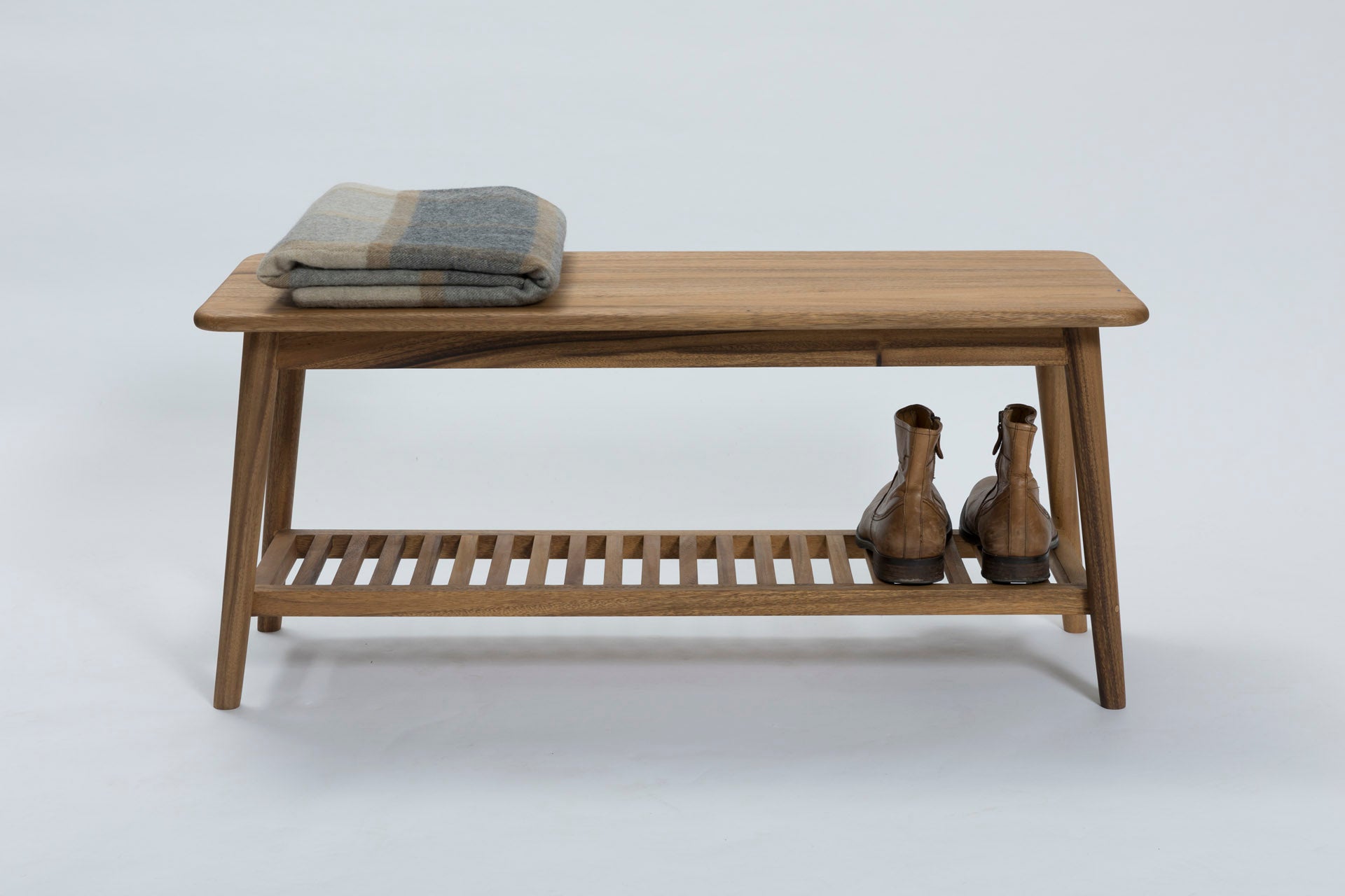Wooden bench with a slatted lower shelf, a folded plaid blanket on top, and a pair of brown boots on the shelf.
