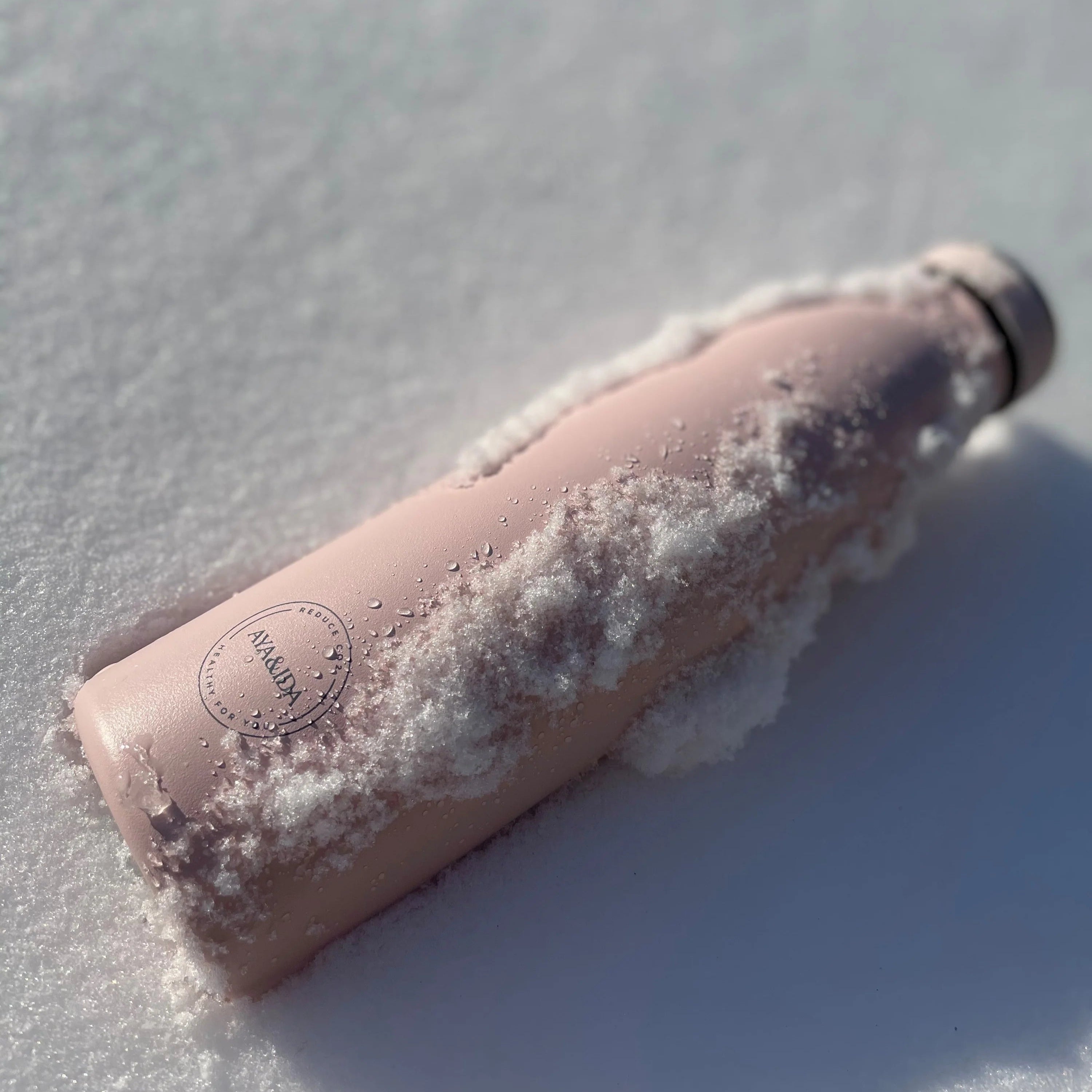 Pink Aya&Ida water bottle covered in snow and ice. The bottle has a minimalist logo.