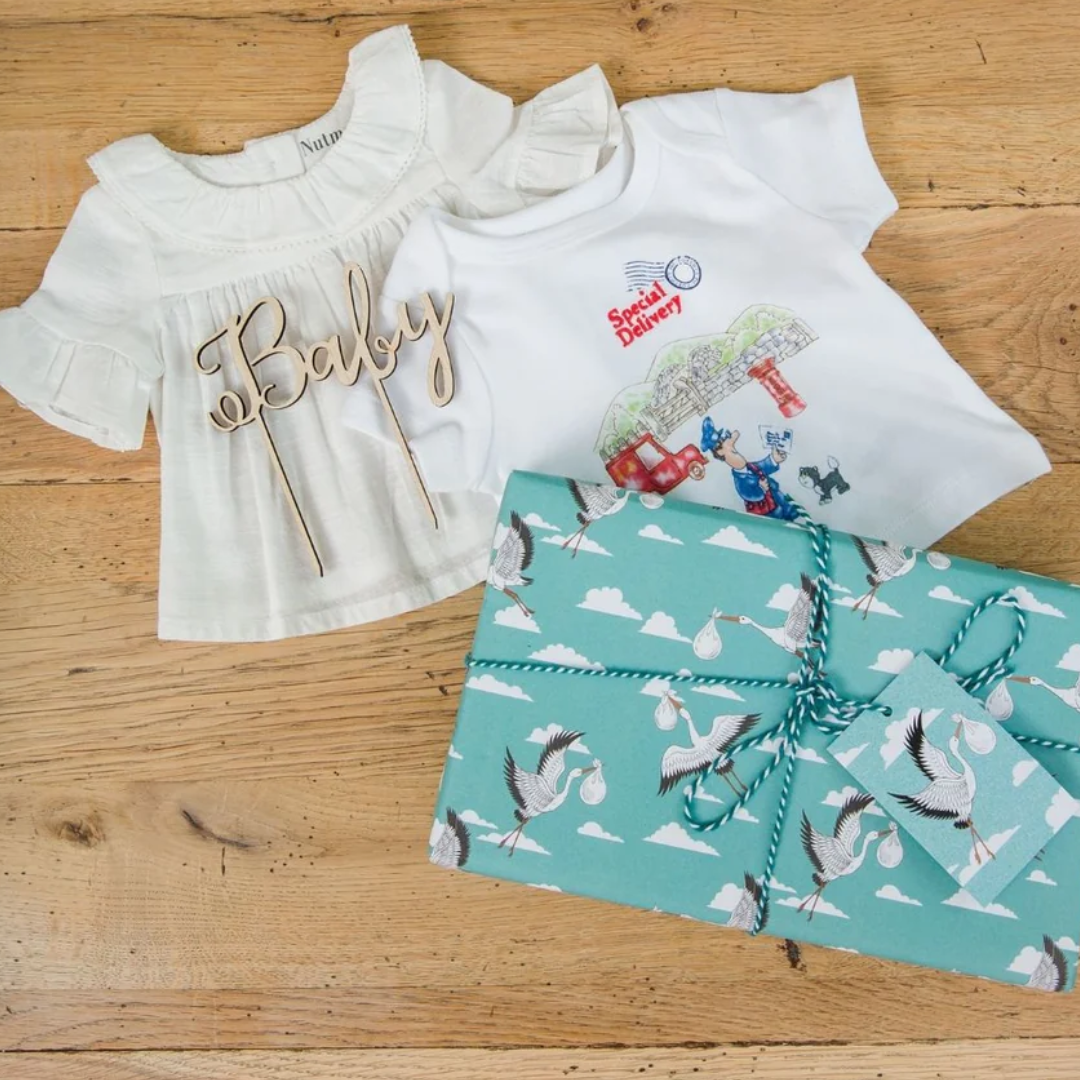 Baby gift set including a white babygrow, a white top, and a teal gift wrapped present with stork design.