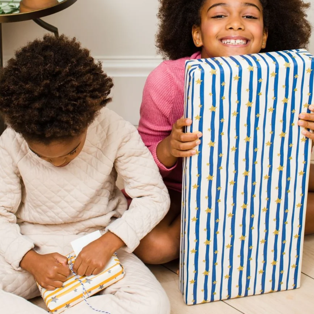 Two children opening gifts wrapped in striped paper with gold stars.  One gift is larger than the other.