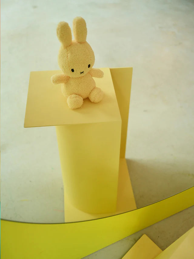 Small plush toy rabbit on a yellow block with a reflective surface below