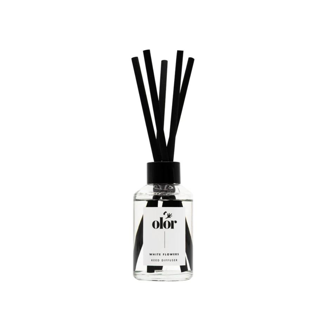 Clear glass reed diffuser bottle with black reeds and "olor" label, indicating "White Flowers" scent.
