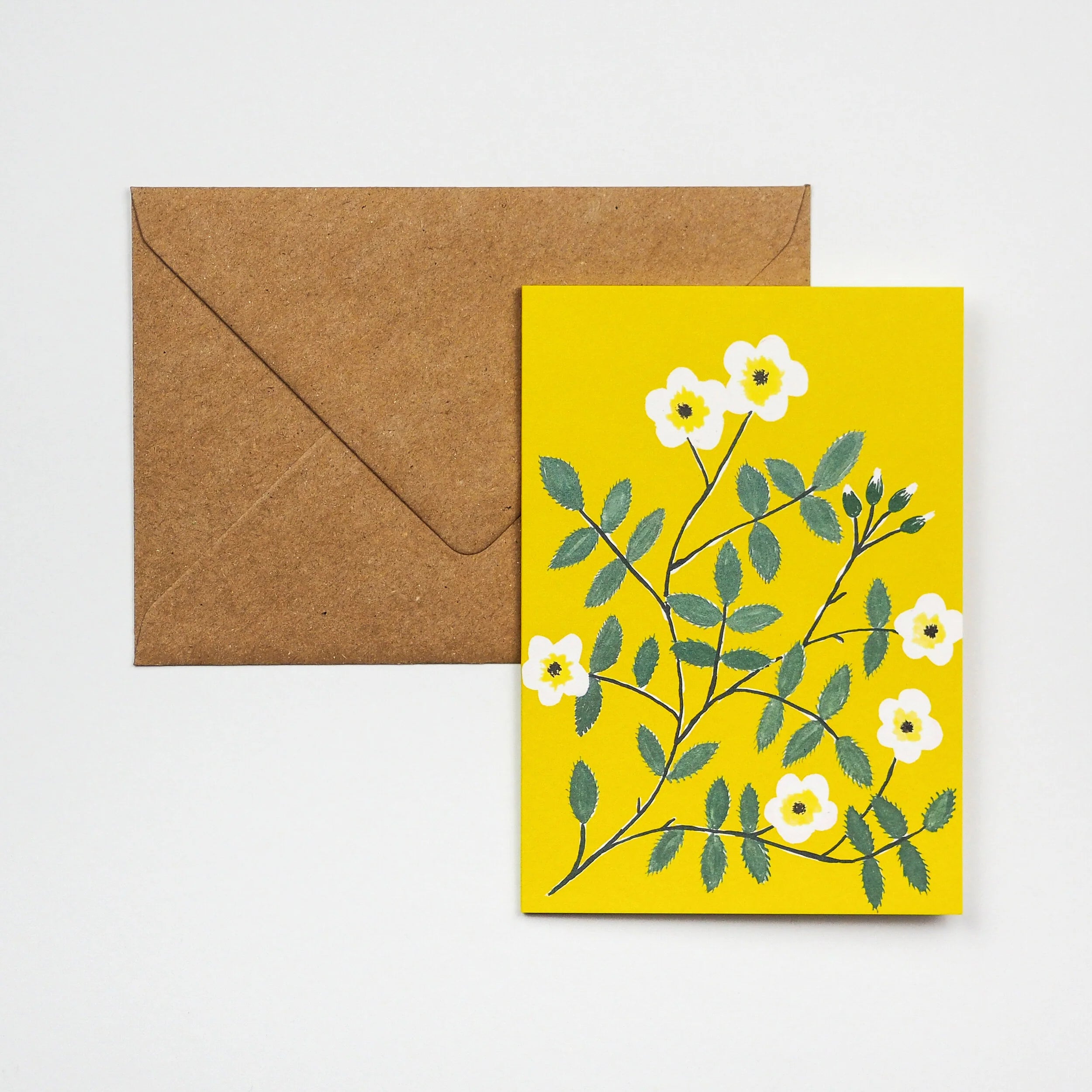 Yellow greeting card featuring a stylized illustration of white flowers and green leaves on a branch.