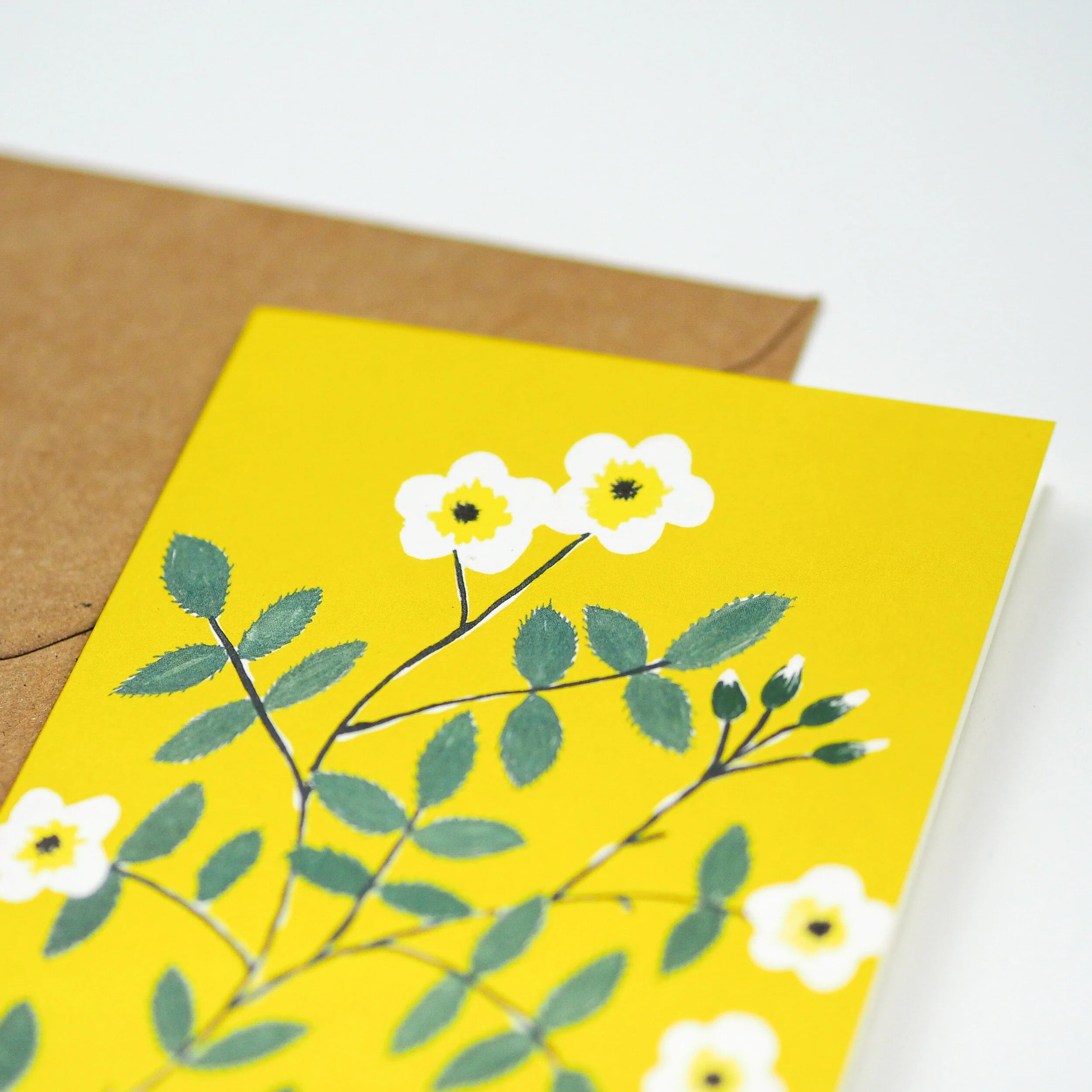 Yellow greeting card featuring a stylized floral pattern of white flowers with yellow centers and green leaves.