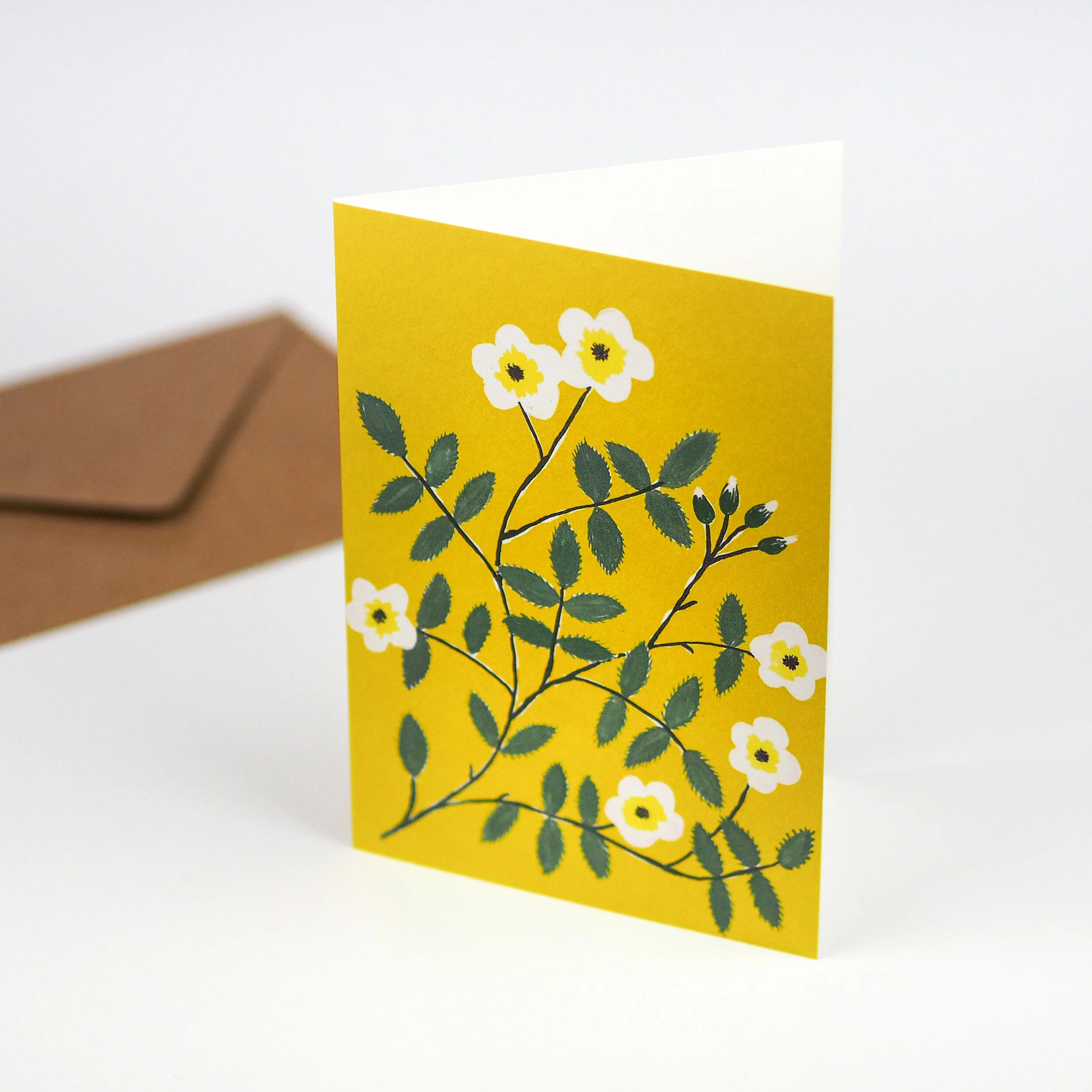 Yellow greeting card featuring a stylized illustration of white flowers and green leaves on a branch.