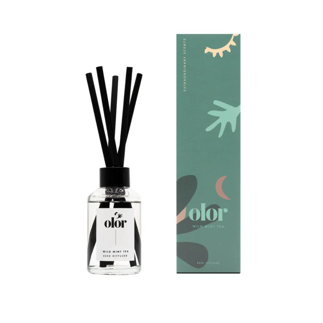 Olor Wild Mint Tea Reed Diffuser.  Clear glass bottle with black reeds, sitting beside its teal and green packaging.