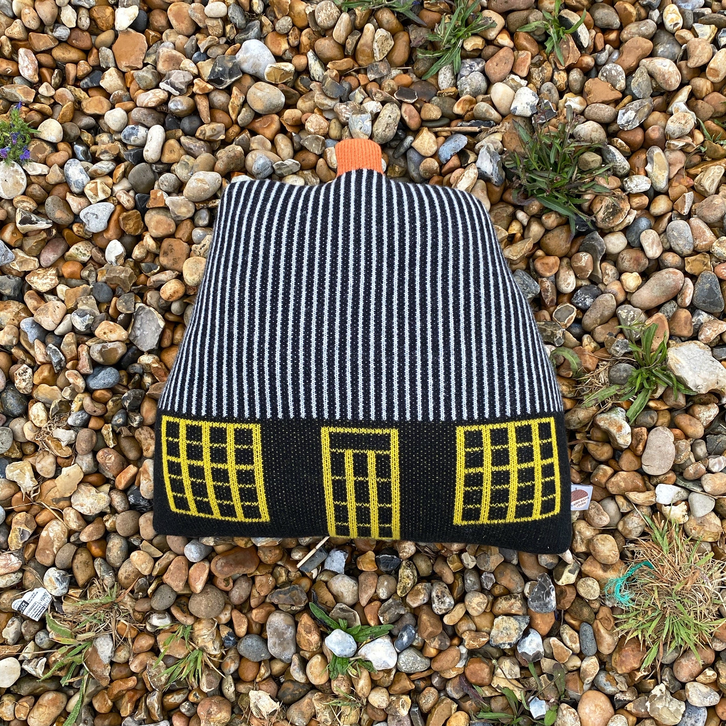 Striped black and white house-shaped cushion by Donna Wilson, featuring yellow windows and an orange top.