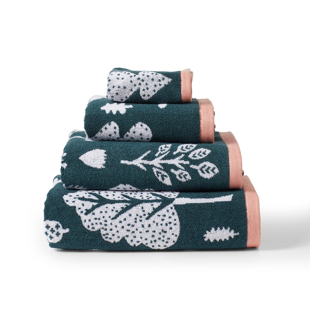 Stack of Donna Wilson towels in dark green with white leaf patterns and peach accents.
