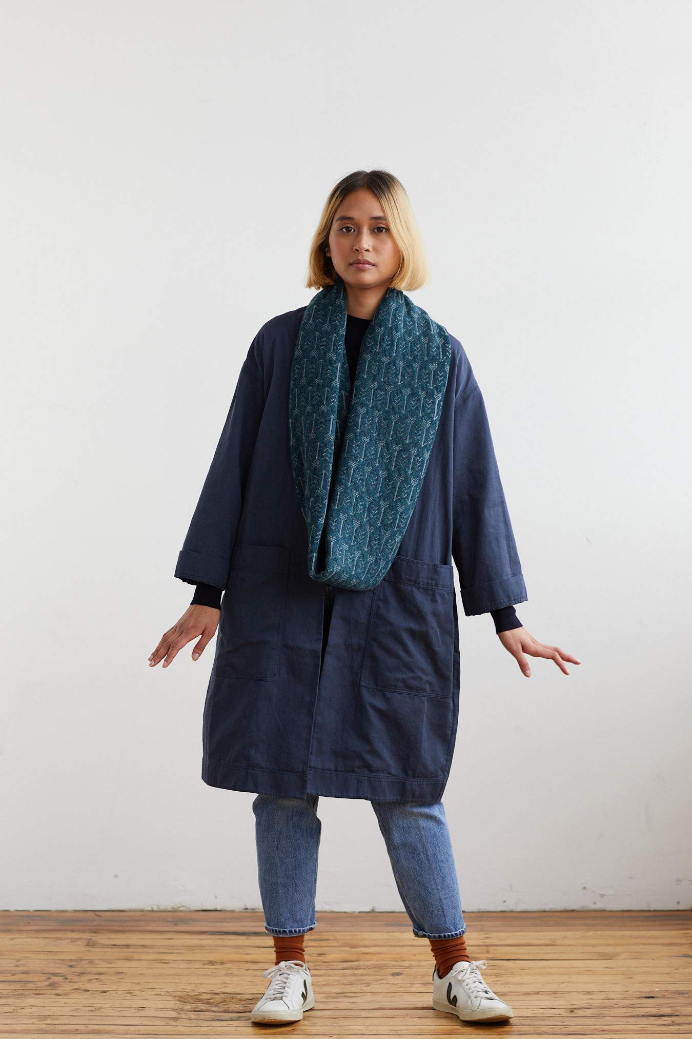 Teal infinity scarf with a subtle repeating pattern, worn by a model over a dark navy coat.