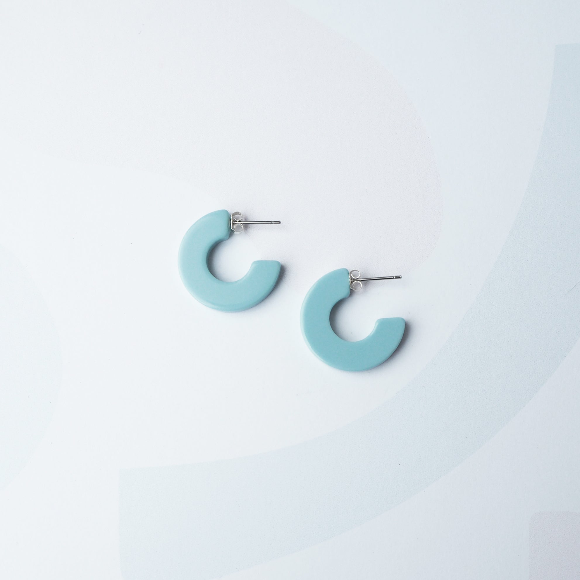 Pair of light blue semi-circular hoop earrings with silver posts.
