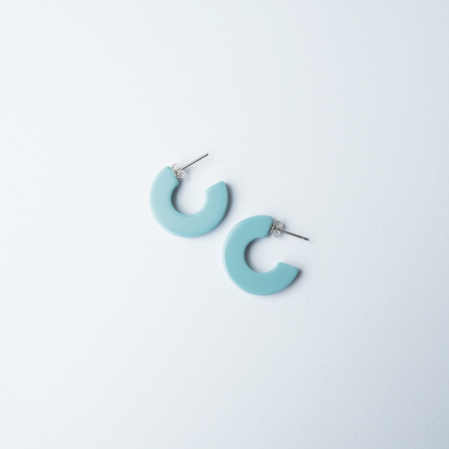 Pair of light blue, semi-circular hoop earrings with silver posts.