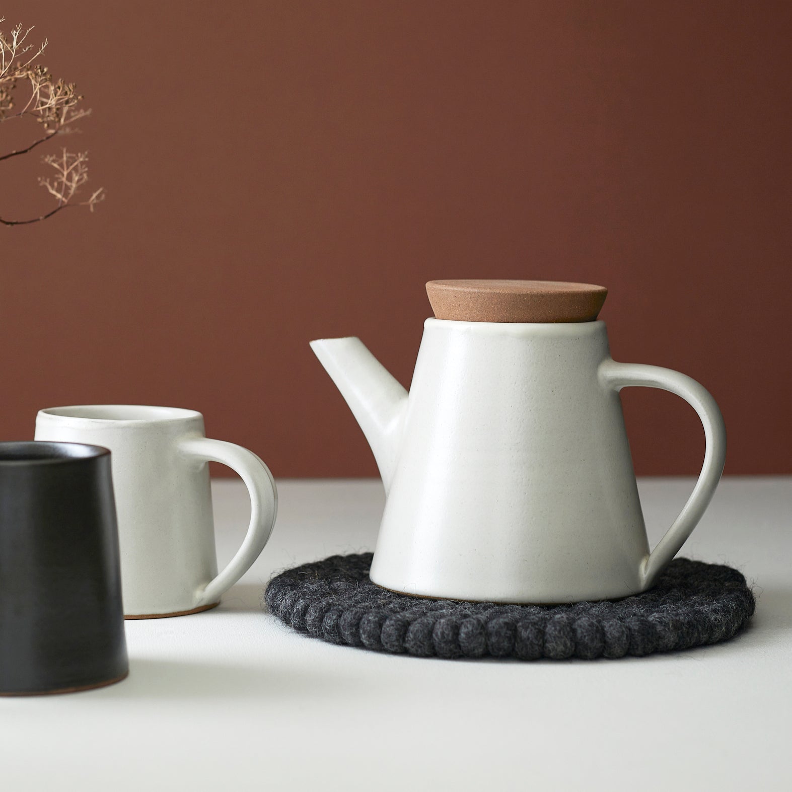 Off-white ceramic teapot with a light brown cork lid, resting on a dark gray felt coaster.