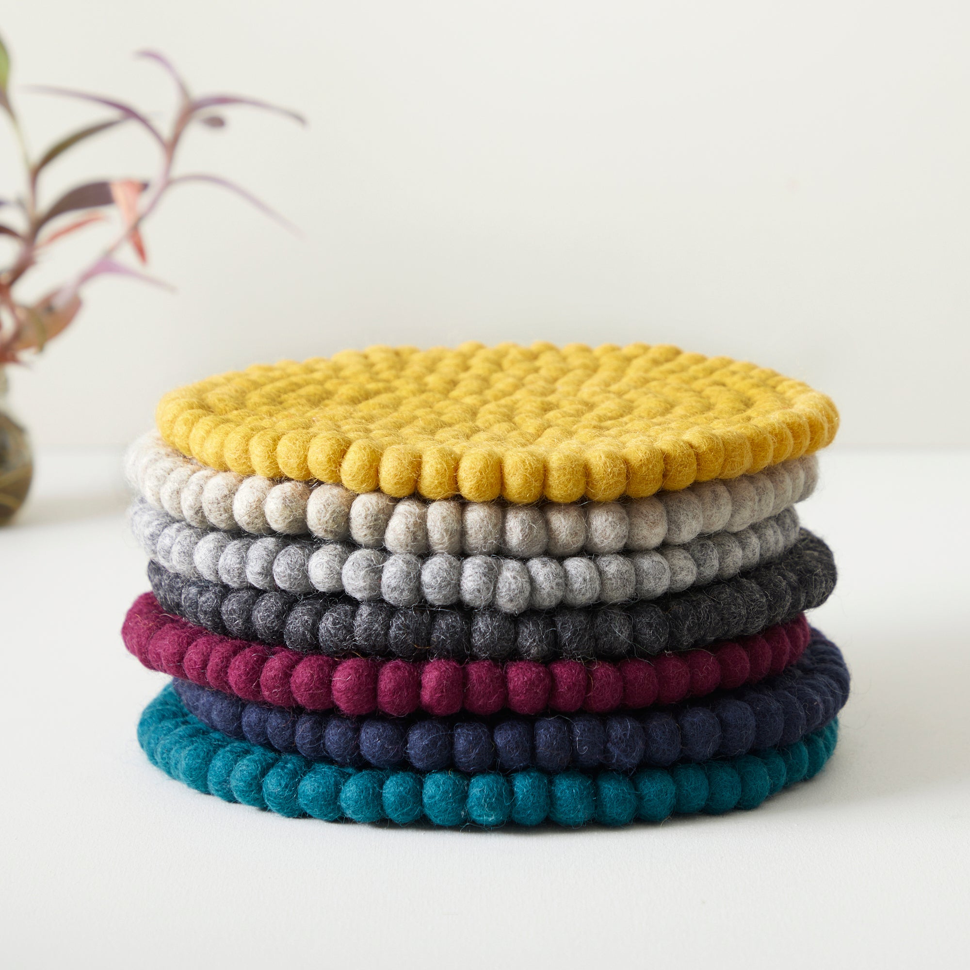 Stack of round felt coasters in various colors, including mustard yellow, gray, dark gray, burgundy, navy, and teal.
