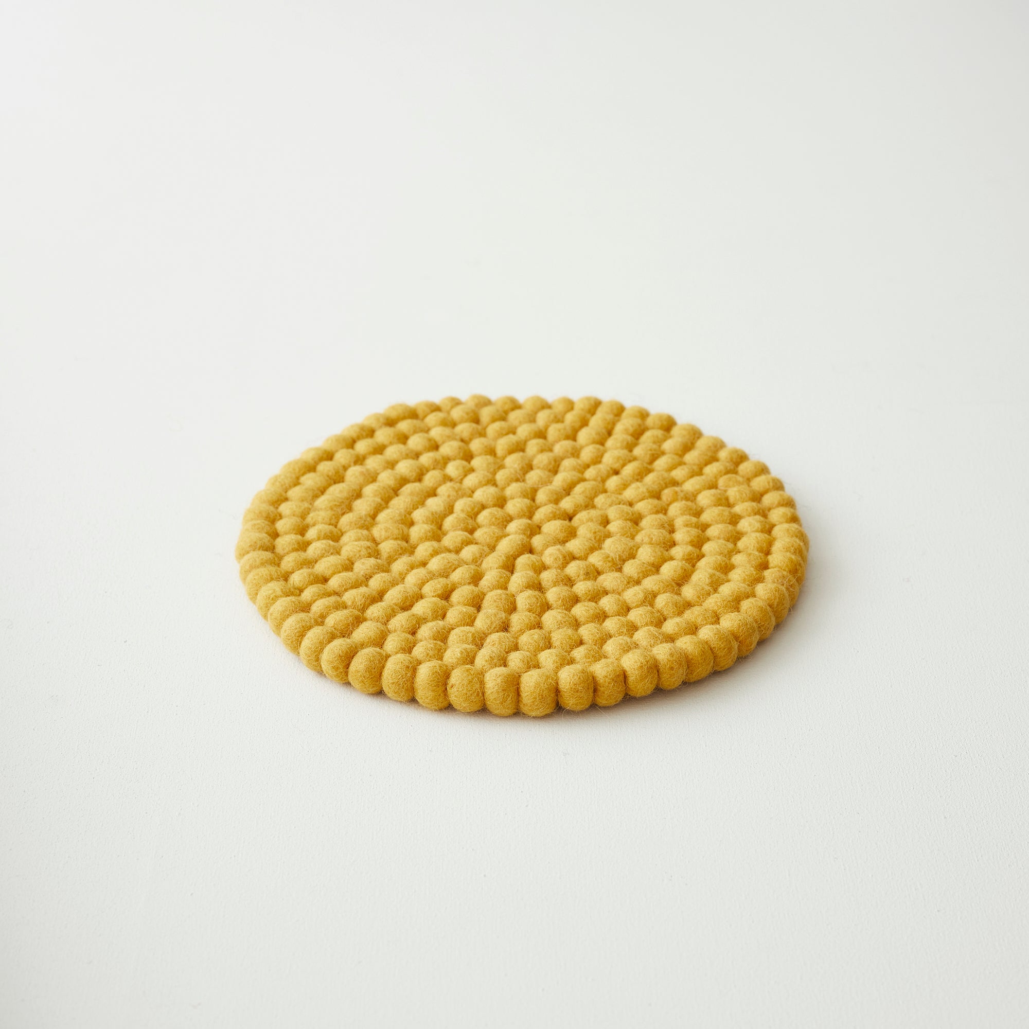 Mustard yellow round felt coaster, composed of small, densely packed felt balls.