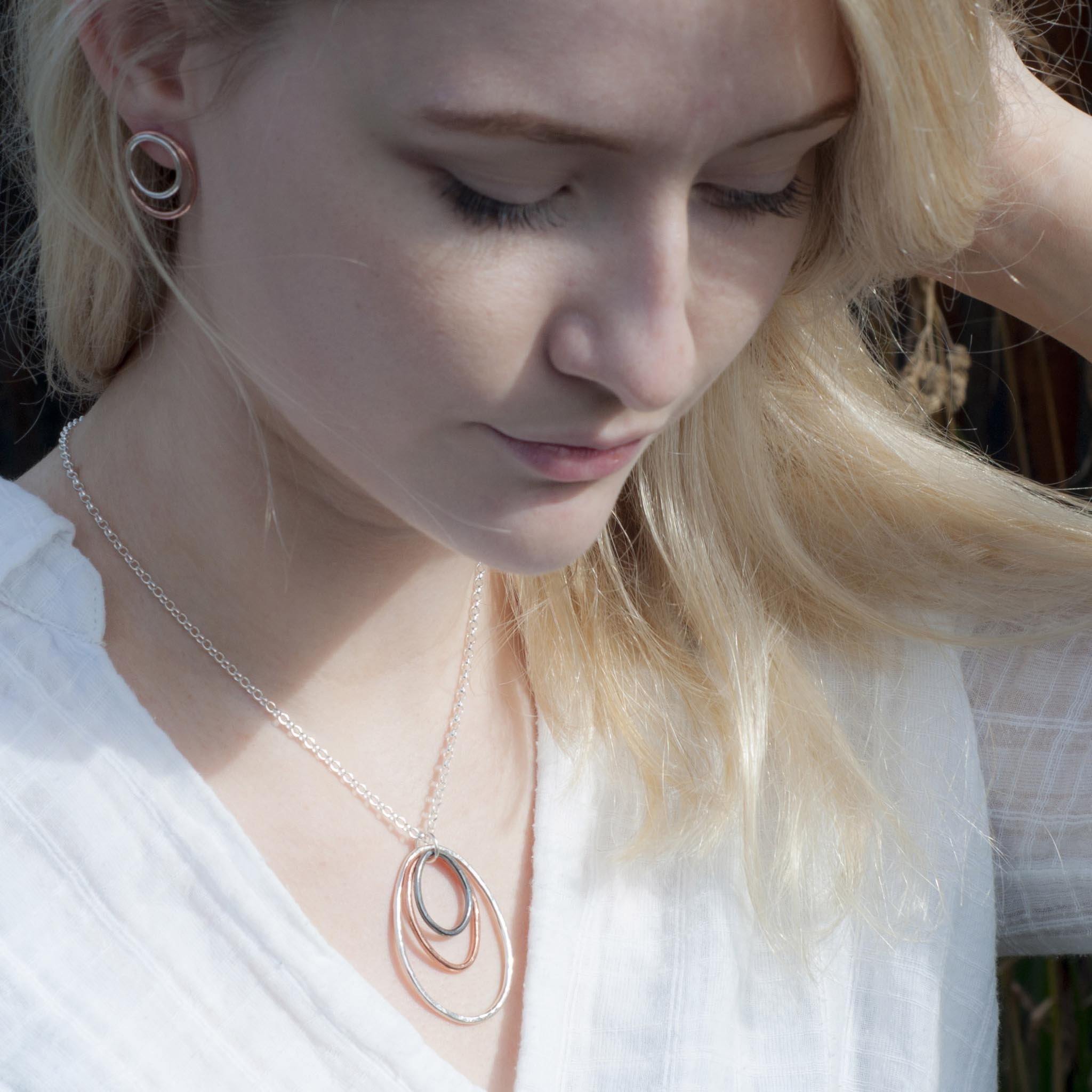 Silver chain necklace with three overlapping oval pendants in silver, rose gold, and dark metal.