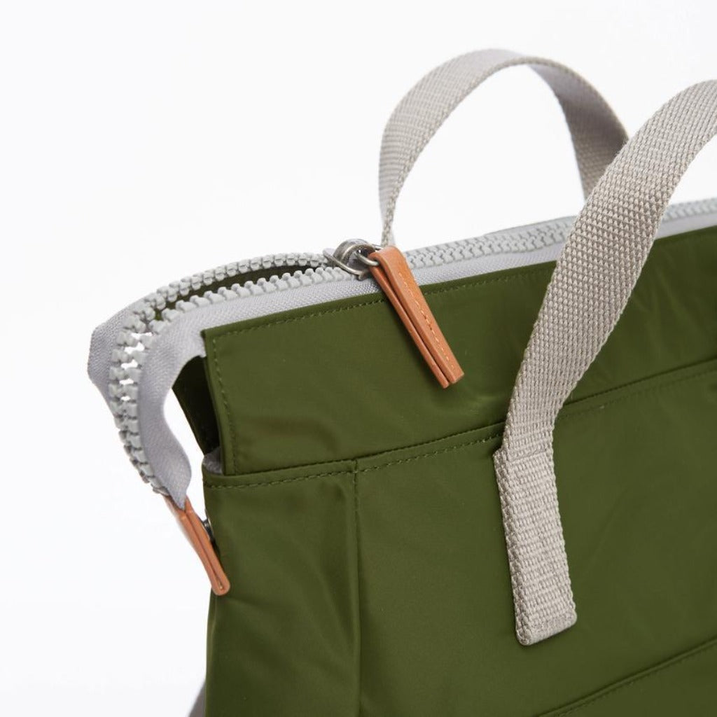 Olive green tote bag with light grey straps and a tan zipper pull. Features a top zipper closure and multiple pockets.