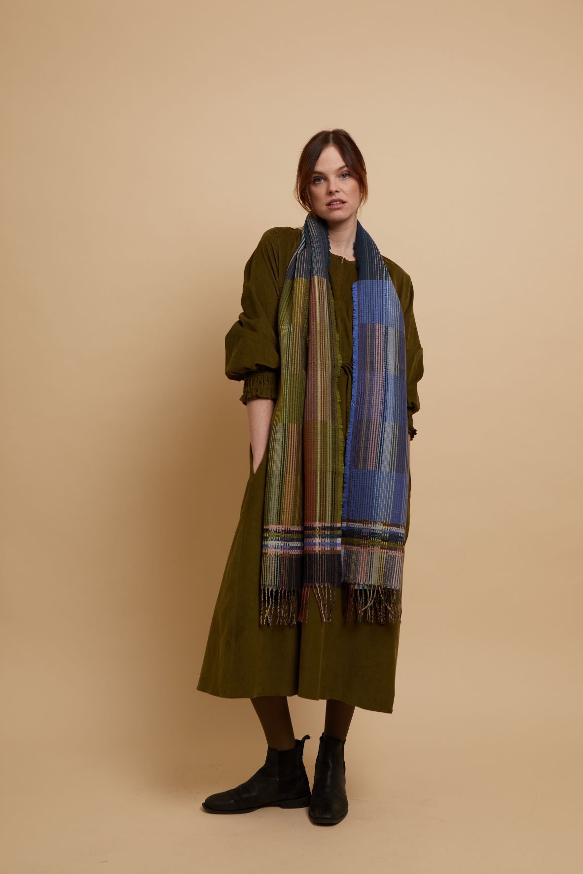 Multicolored woven scarf with fringed edges; predominantly blues, greens, and browns in a plaid pattern.