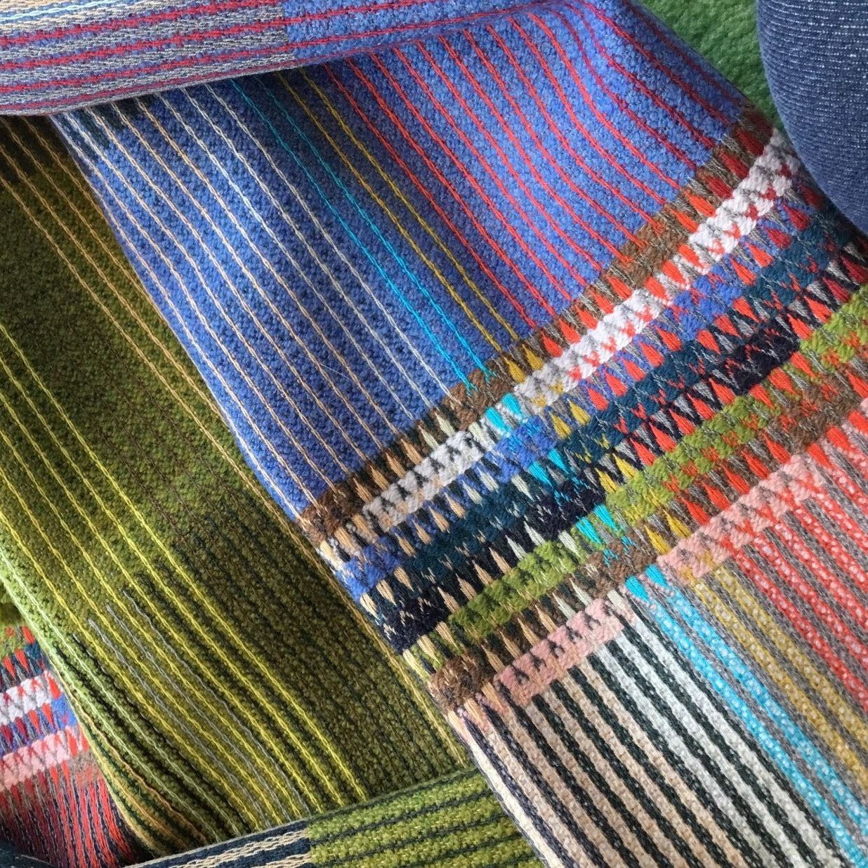 Close-up of multicolored woven textile with vertical stripes and intricate patterned sections in blues, greens, reds, and