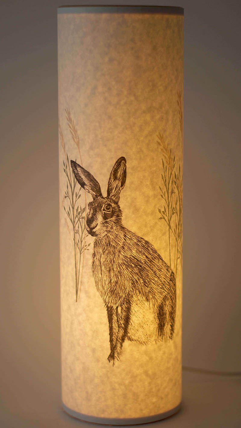 Cylindrical lampshade with a grayscale illustration of a hare sitting amidst grasses.