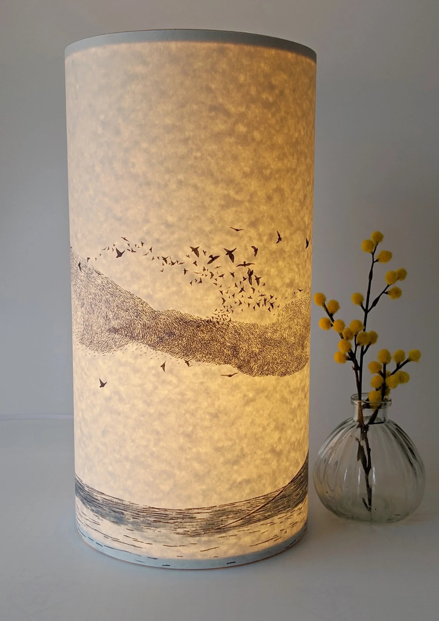 Illuminated cylindrical lampshade with a flock of birds and landscape design.
