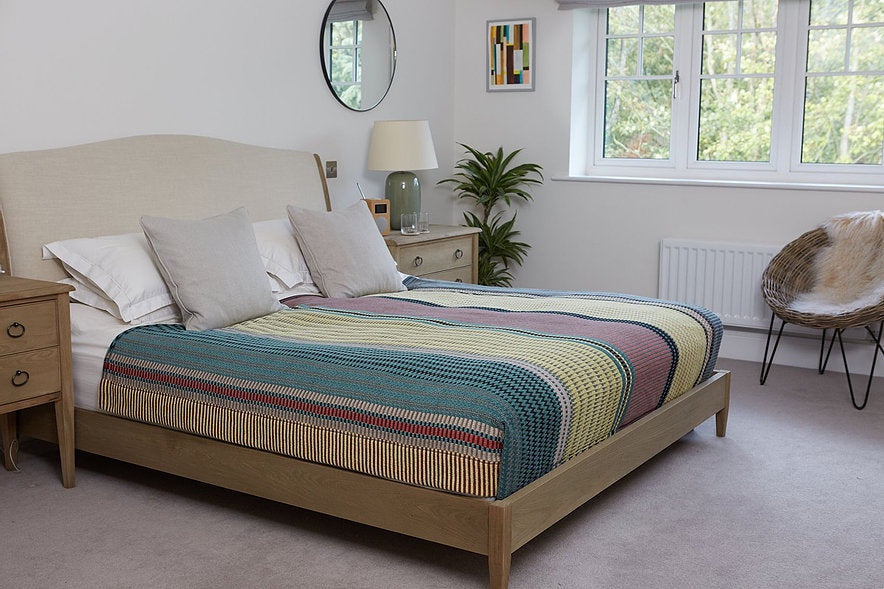 Light wood double bed with beige headboard and multicolored striped throw blanket.