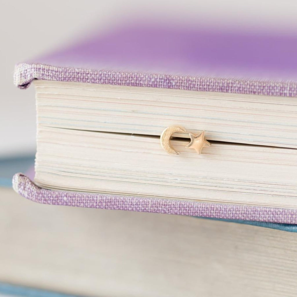 Gold crescent moon and star bookmark nestled in the pages of a lavender book.