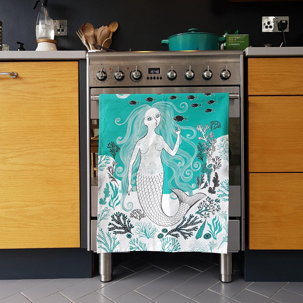 Teal kitchen towel depicting a mermaid with flowing hair, surrounded by sea life and coral.