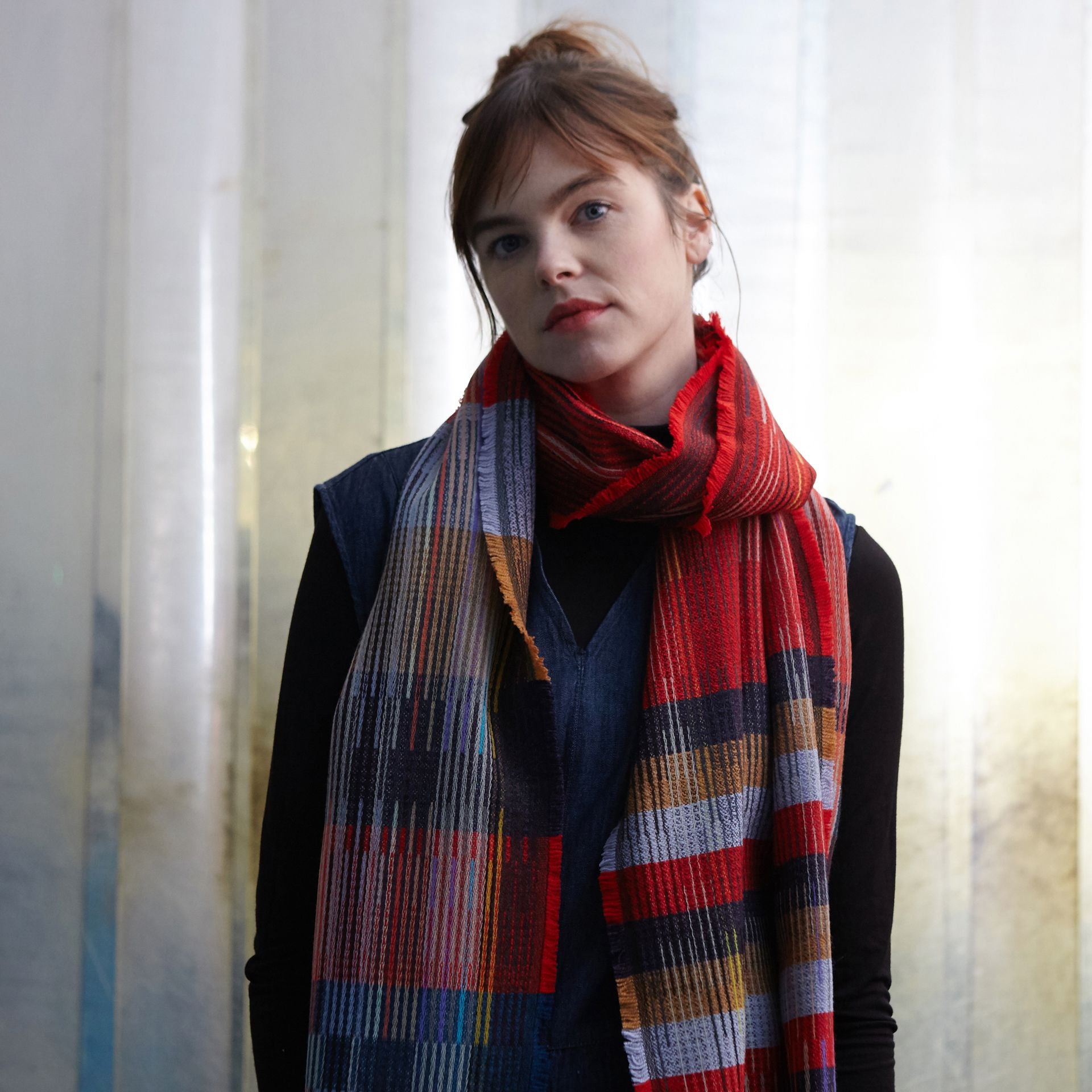 Red, multicolored woven scarf with frayed edges, featuring stripes and blocks of color in varying shades of red, blue, tan,