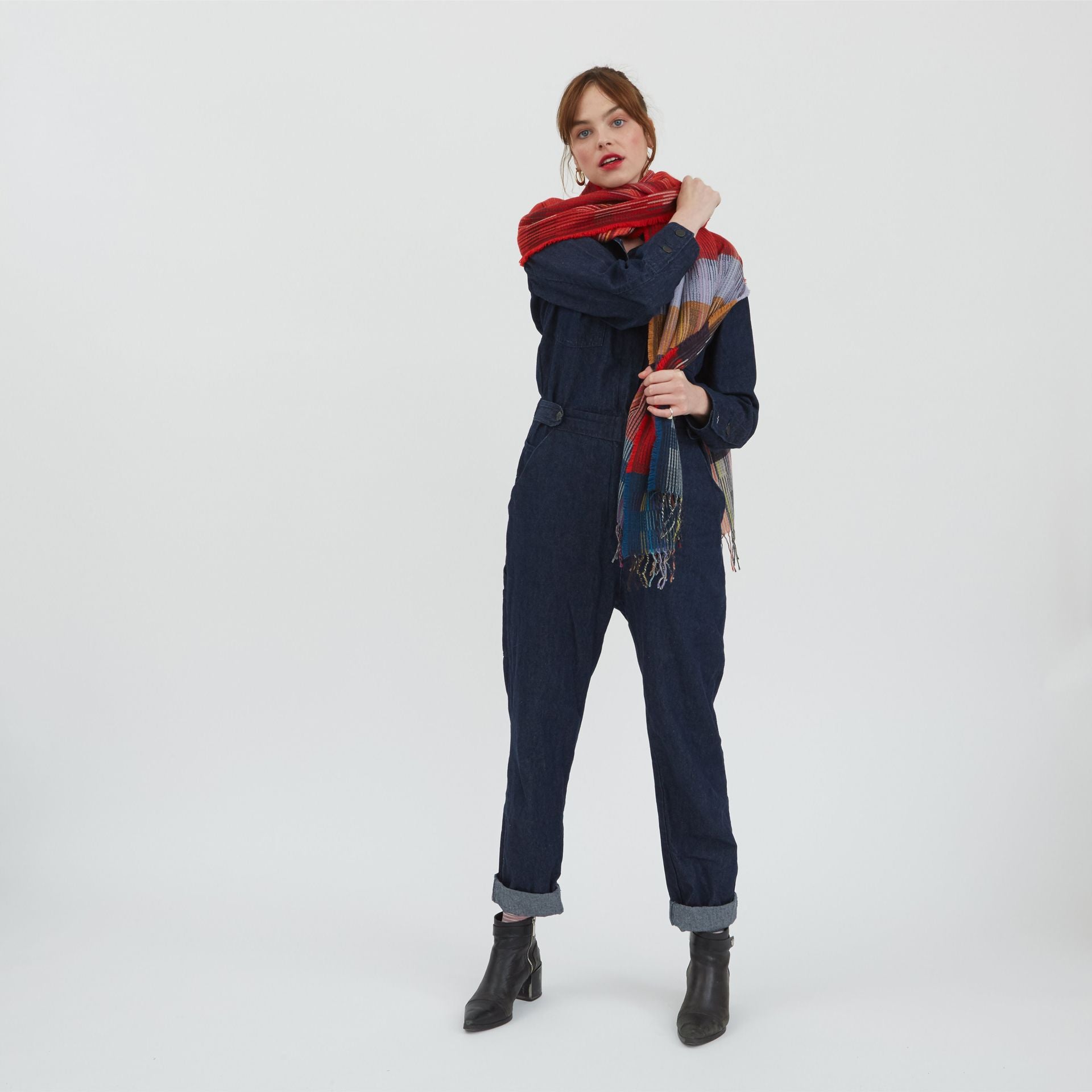 A woman models a dark denim jumpsuit and a multicolored striped scarf with red, blue, and beige stripes.