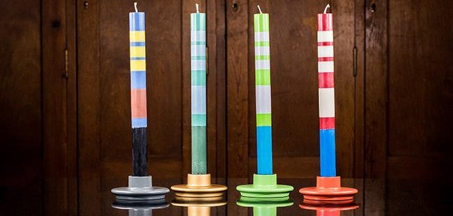 four striped, multi-coloured British Colour Standard candles in small wooden candleholders