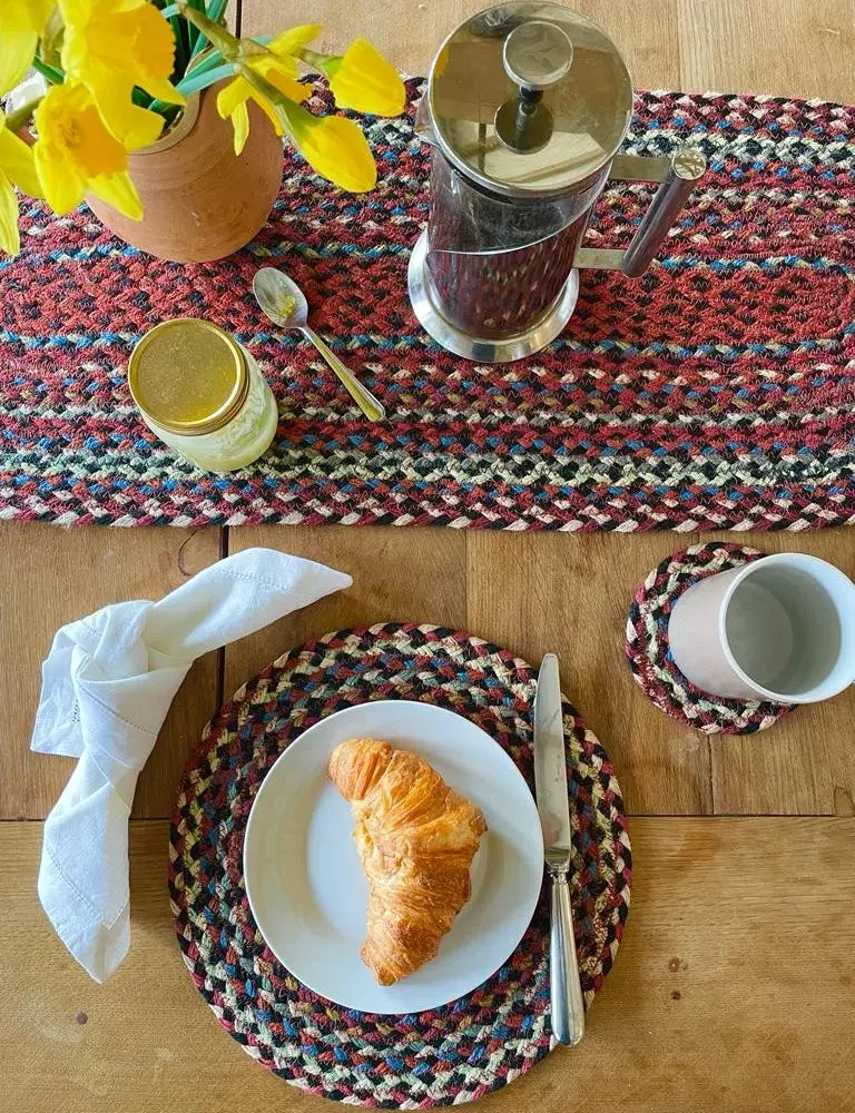 an aerial view of a breakfast table, showing a table runner. coaster, and  placemat, made of jute, manufactured by the braided rug company