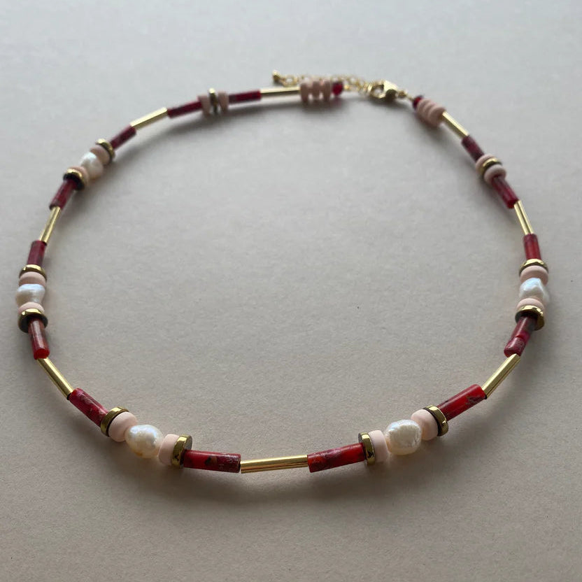 Necklace with red, gold, and pearl beads on a light gray background