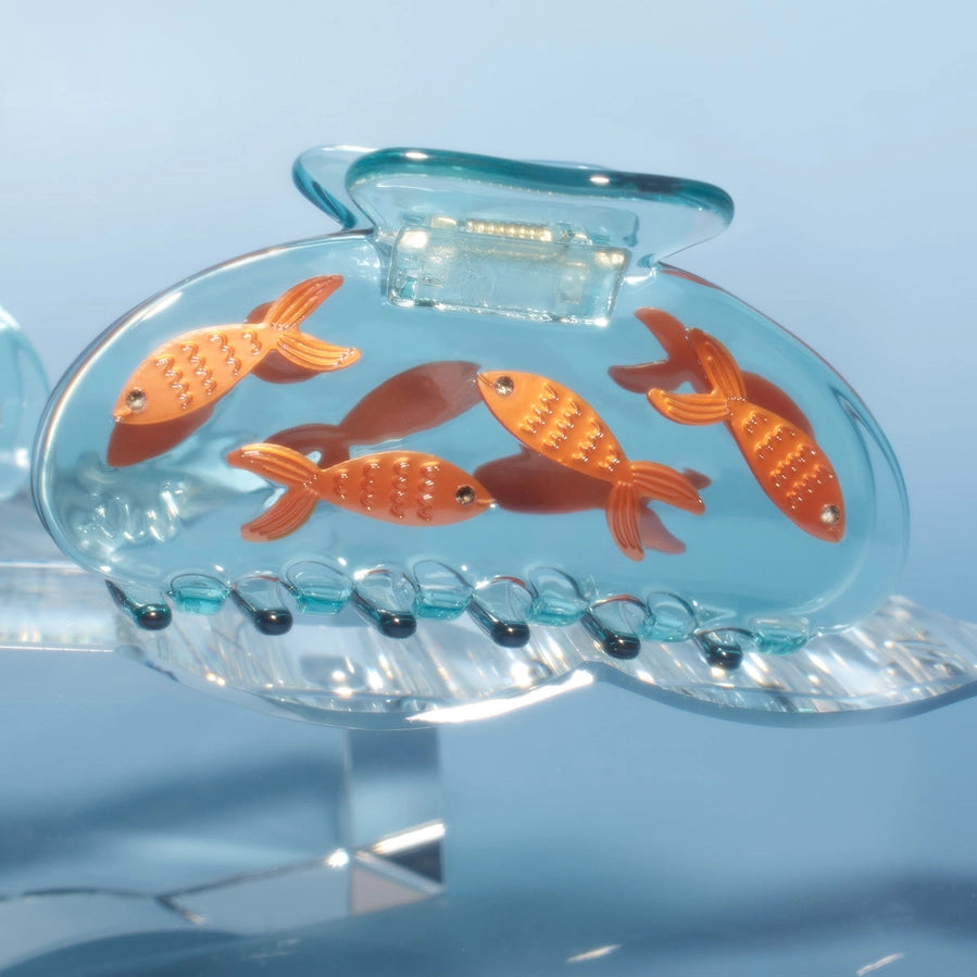 Clear plastic hair clip with orange fish on a light blue background
