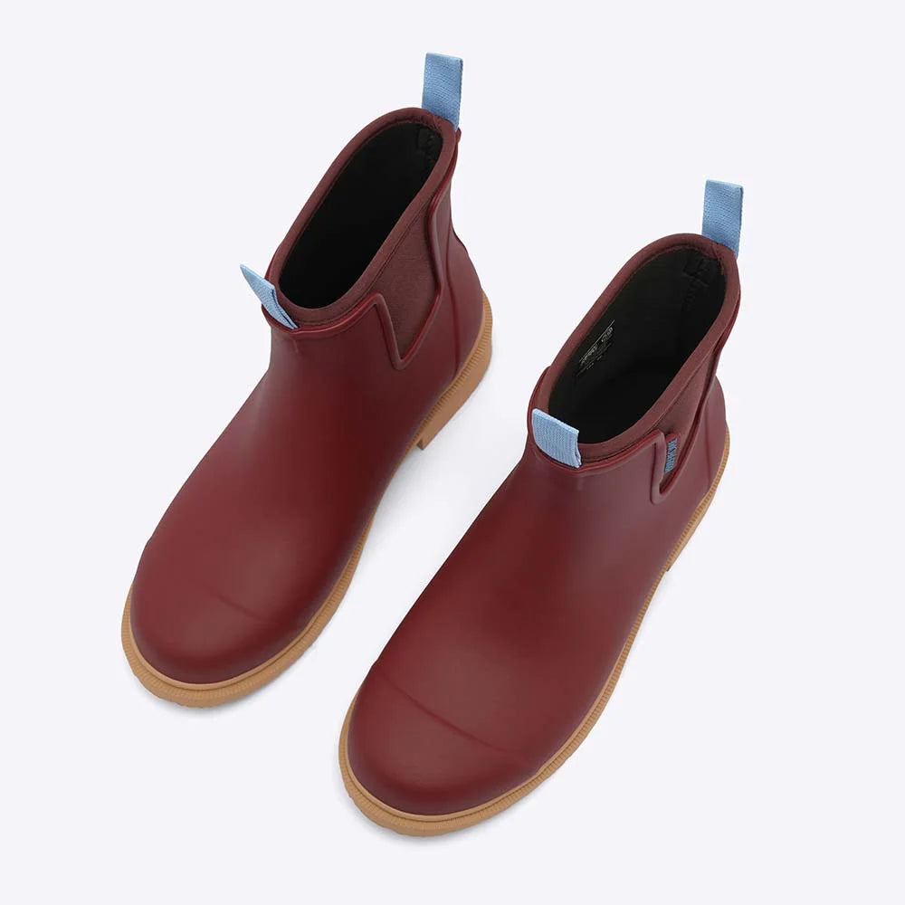 Pair of red rubber boots with brown soles on a white background