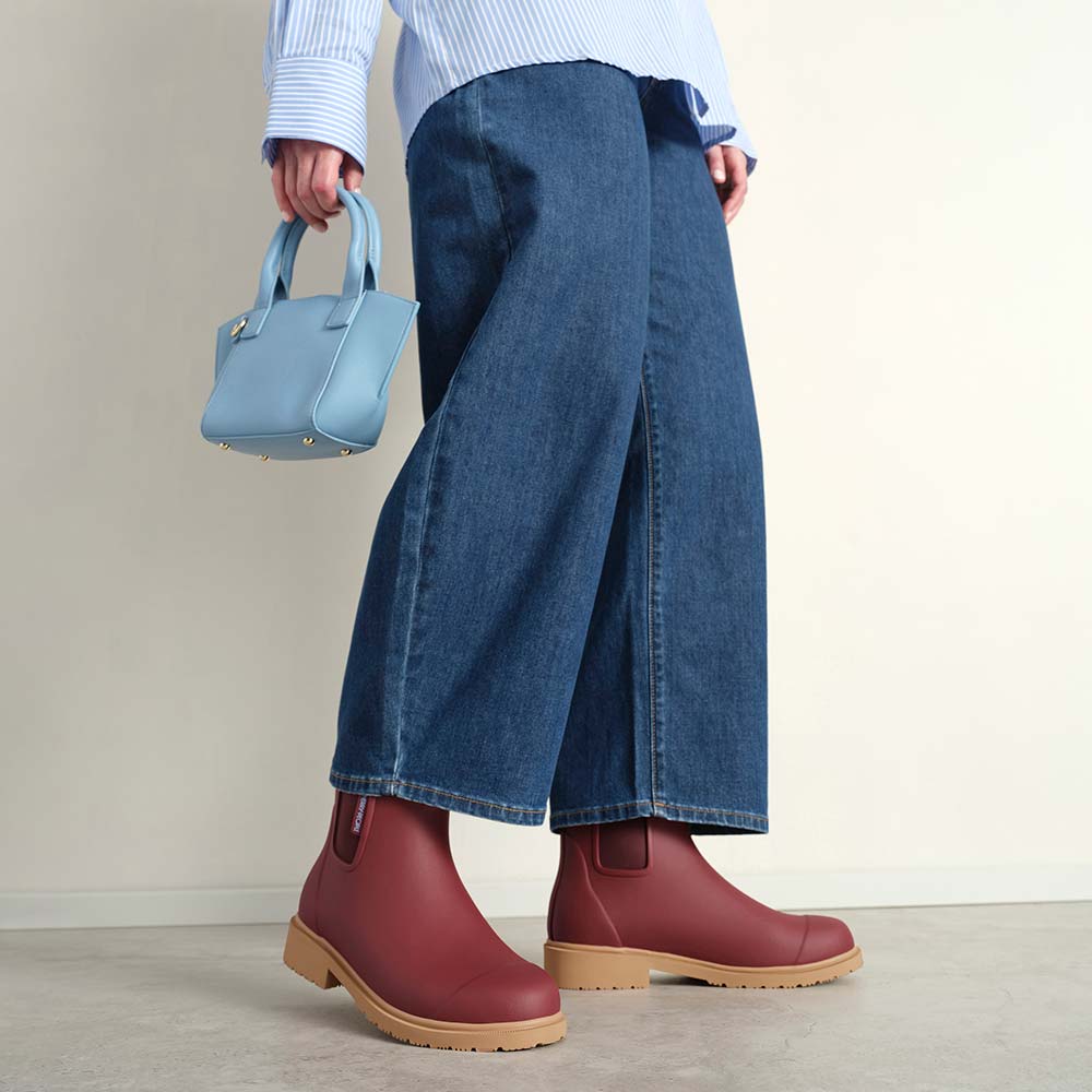 Person wearing red boots, blue jeans, and a light blue handbag on a neutral background