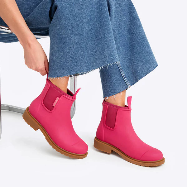 Person wearing bright pink ankle boots with brown soles on a white background