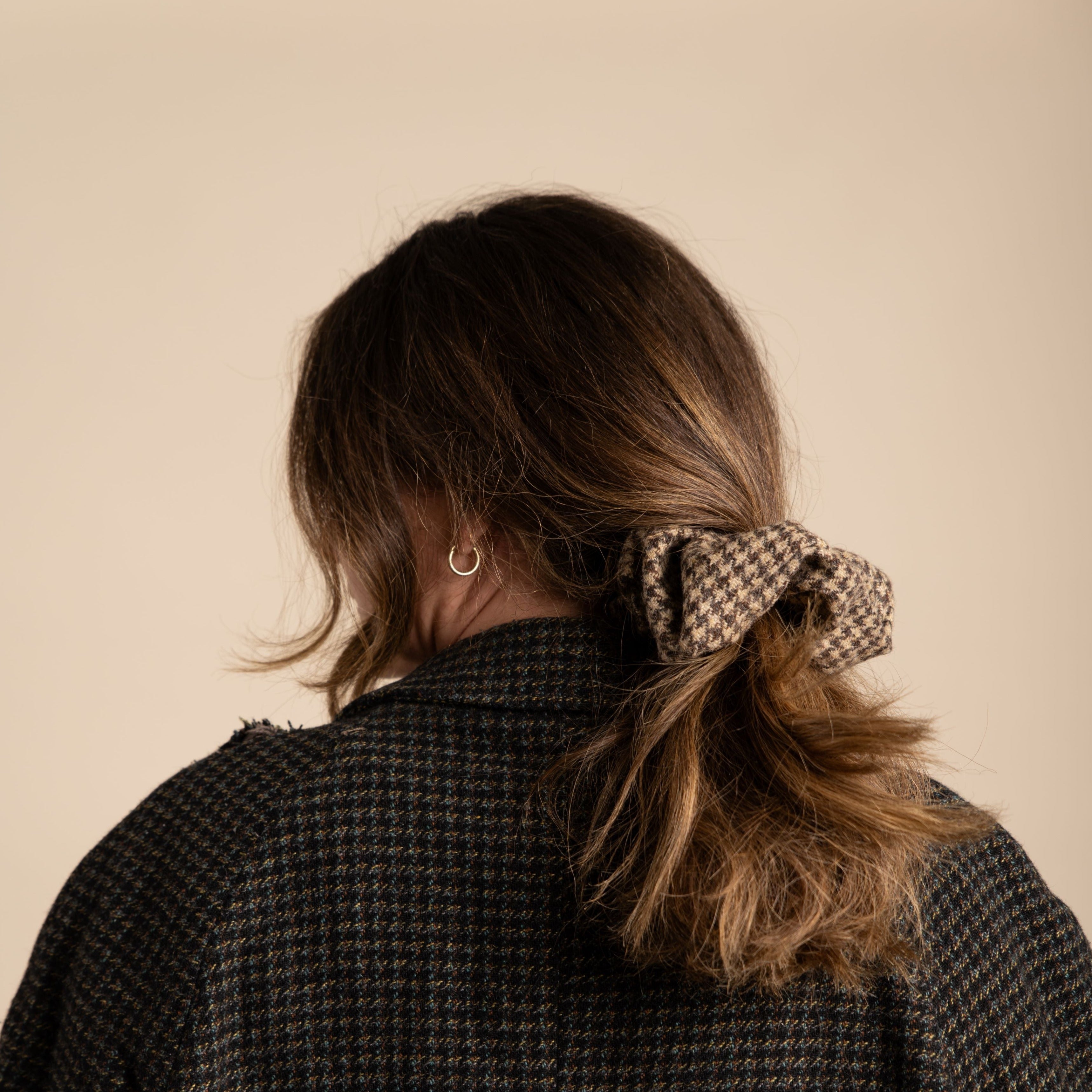 Brown and beige houndstooth hair scrunchie in a woman's brown hair, pulled back in a low ponytail.