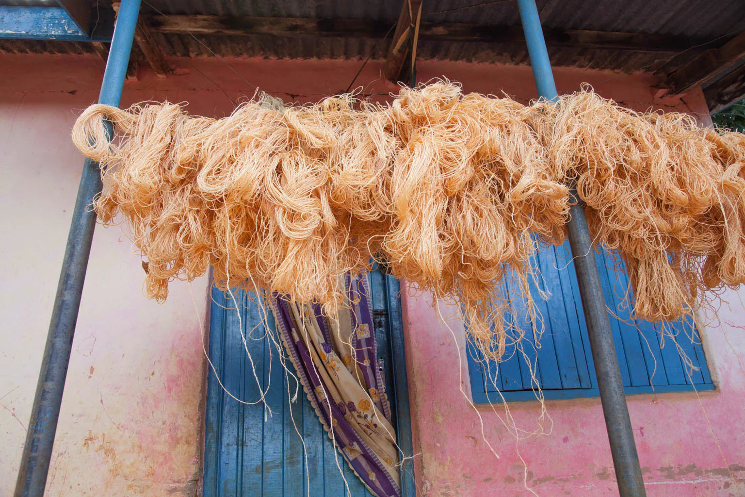 Large bundles of light orange string or yarn hang drying from metal poles outside a building.